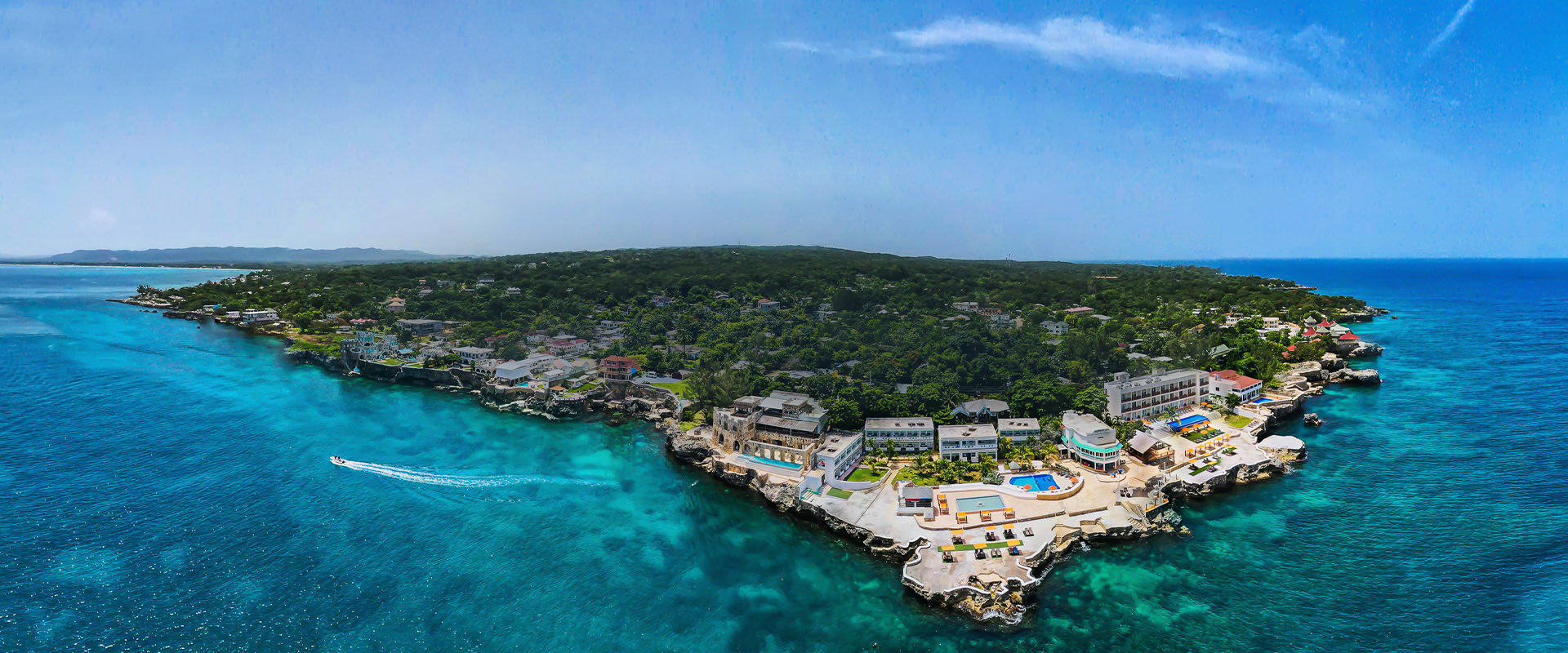 aerial view of resort building with lush tropical trees behind it, view of shape of coast with deep turquoise water