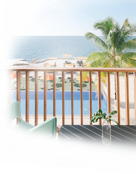 view from guest room balcony of pool with sunbathing cabanas and ocean in background