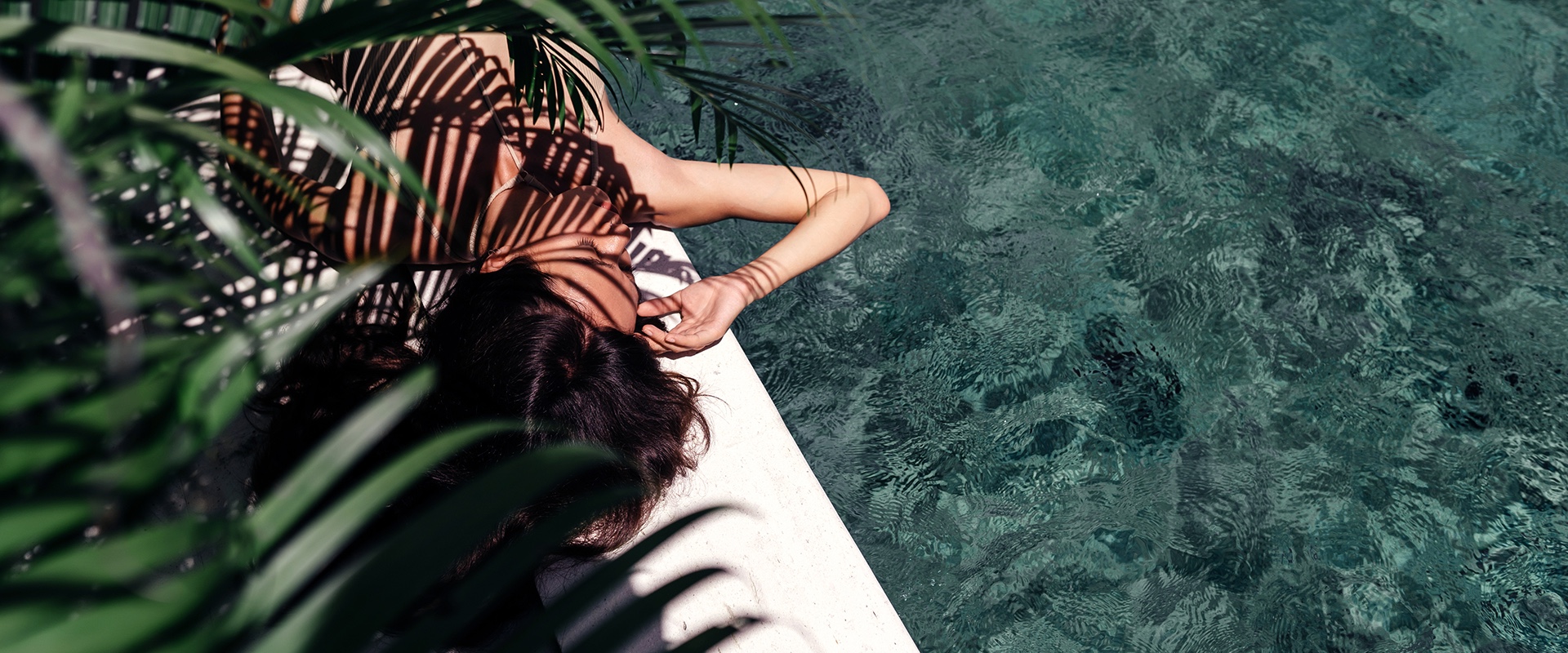 girl lying close to a pool and with a palm shadow on her body