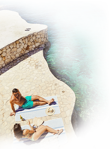 couple in swim suit relaxing while lounging on beach towel on natural stone patio overlooking the ocean