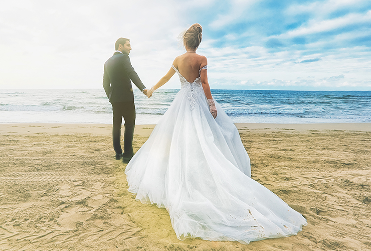 groom leading bride on sand towards ocean 