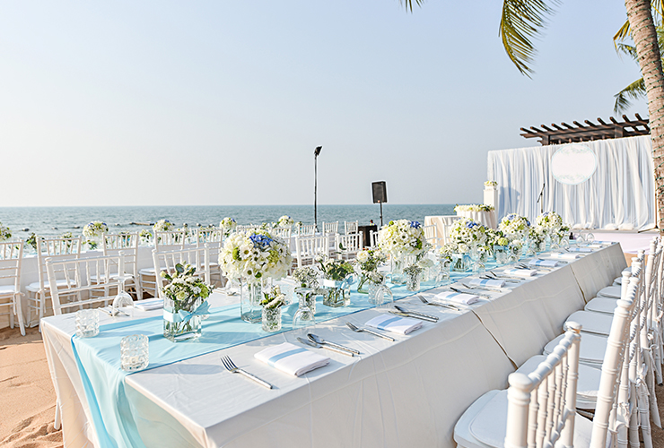 formal white banquet tables set for wedding on beach with view of ocean