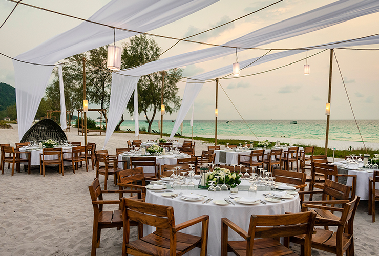 fine dining tables set up on sand with white linens at sunset