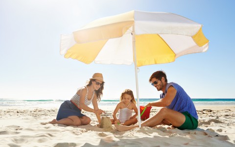 Family sitting on beach under umbrella 