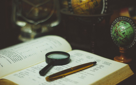 magnifying glass and pen on open book