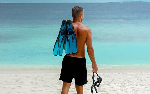 man holding snorkeling gear on beach facing ocean