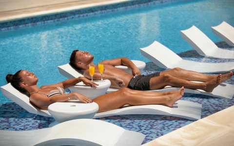 man and woman tanning on waterside pools with mimosas next to them