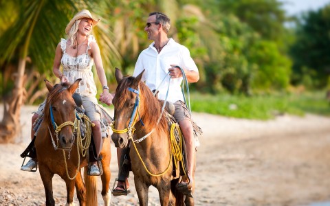 man and woman riding on horses on the beach
