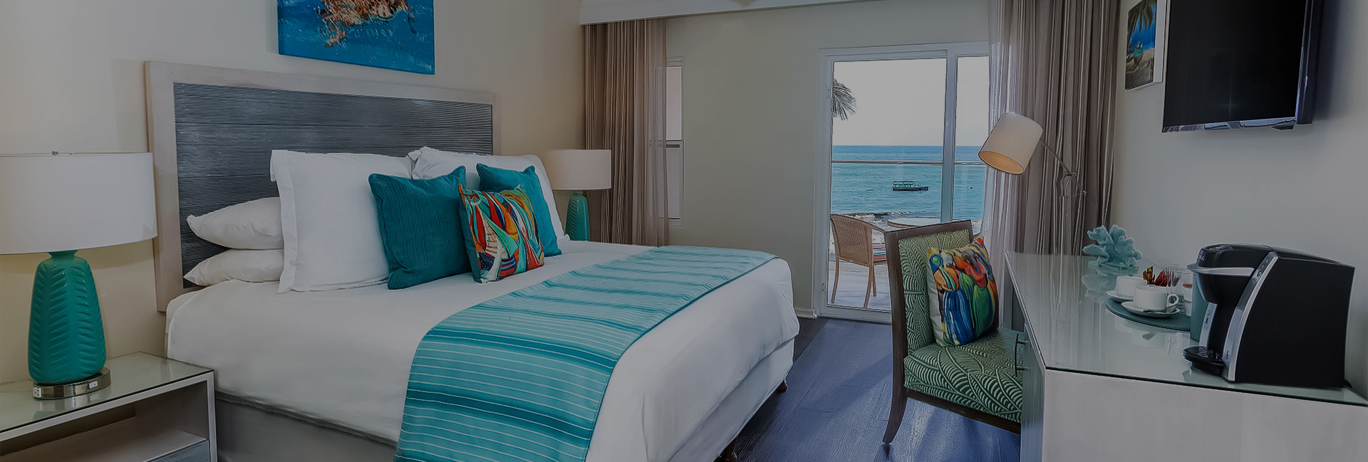 bed with blue pillows and bedrunner with desk across from it with coffee maker on it