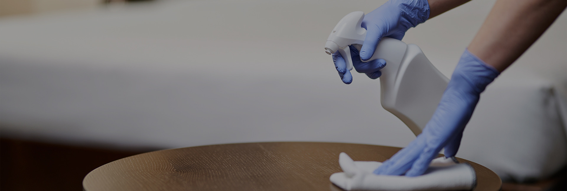 person wearing gloves spraying bottle on table