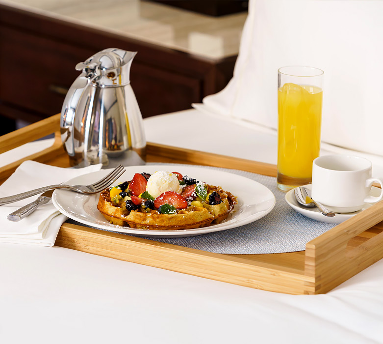 breakfast tray with a belgian waffle with red berries on top, orange juice and coffee
