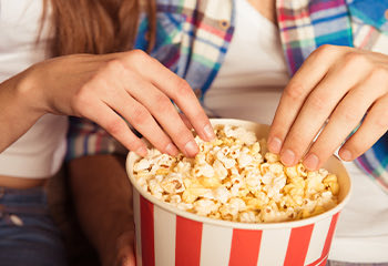 Close up of two hands grabbing pop corn on a red an white bucket
