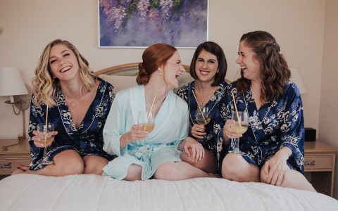 Group of woman in robes having drinks on bed