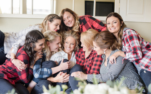 Bride in white pajama being hugged by group of bridesmaids in checkered pajamas
