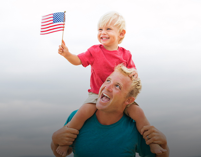 father and son on shoulders smiling holding a flag