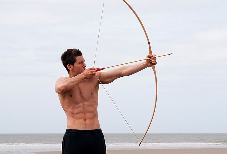 Man using bow and arrow on the beach