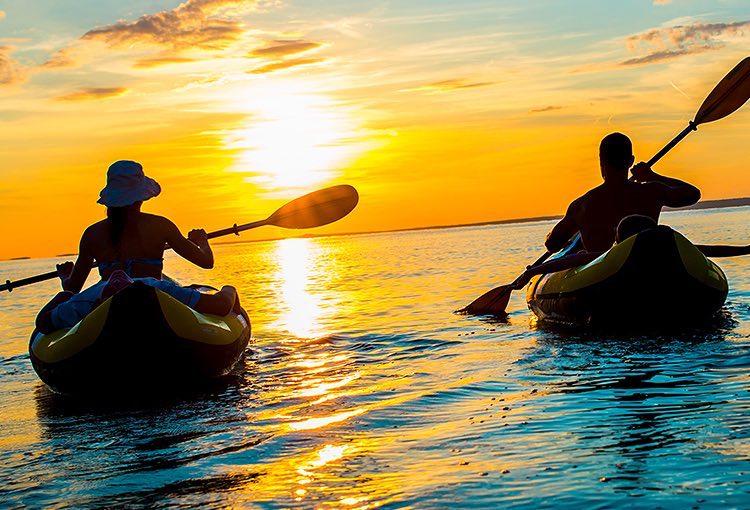 Two people kayaking into the sunset