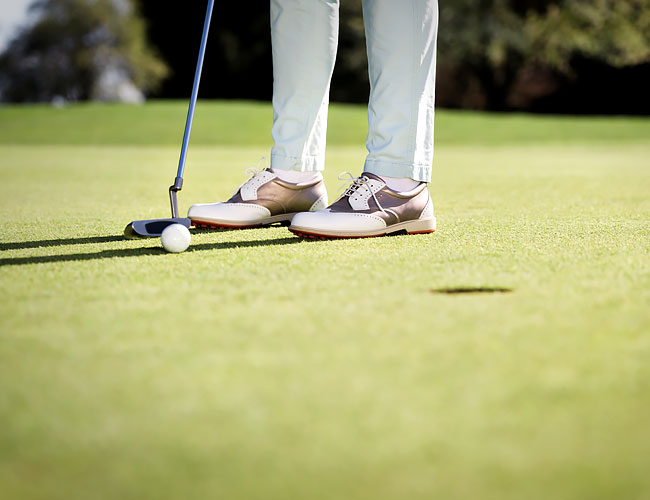 Man wearing golf shoes putting a golf ball into hole