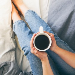 a girl holding a mug filled with coffee on a bed