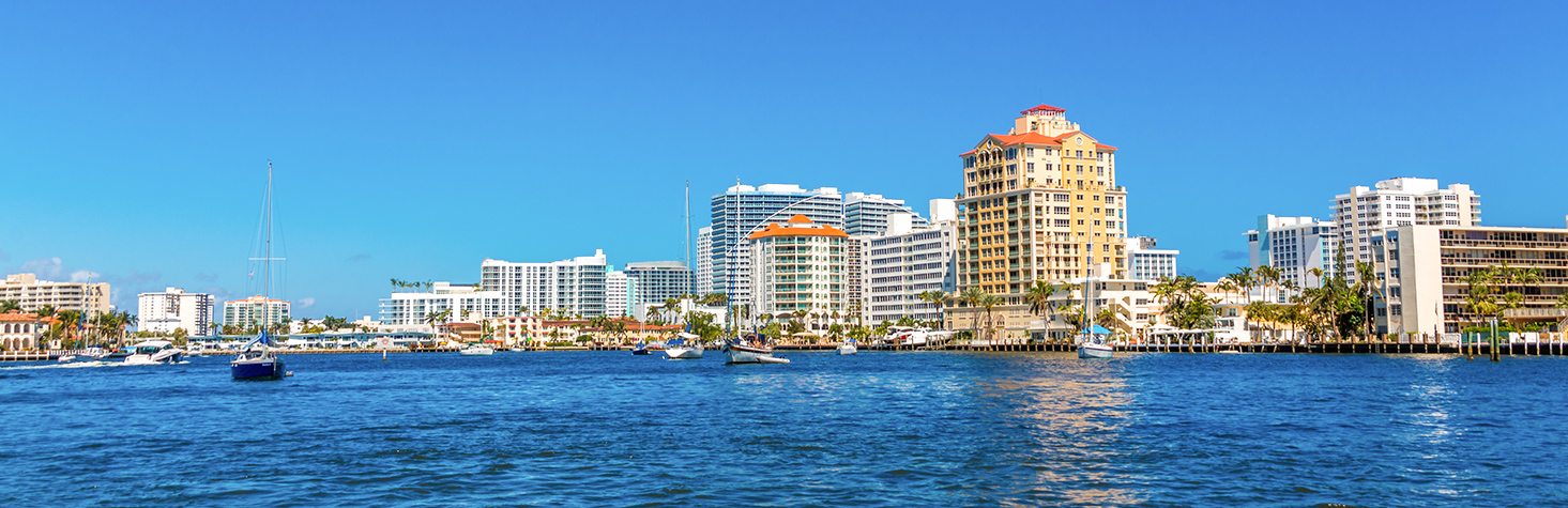 A view of downtown buildings from the ocean water with several sailboats in the water
