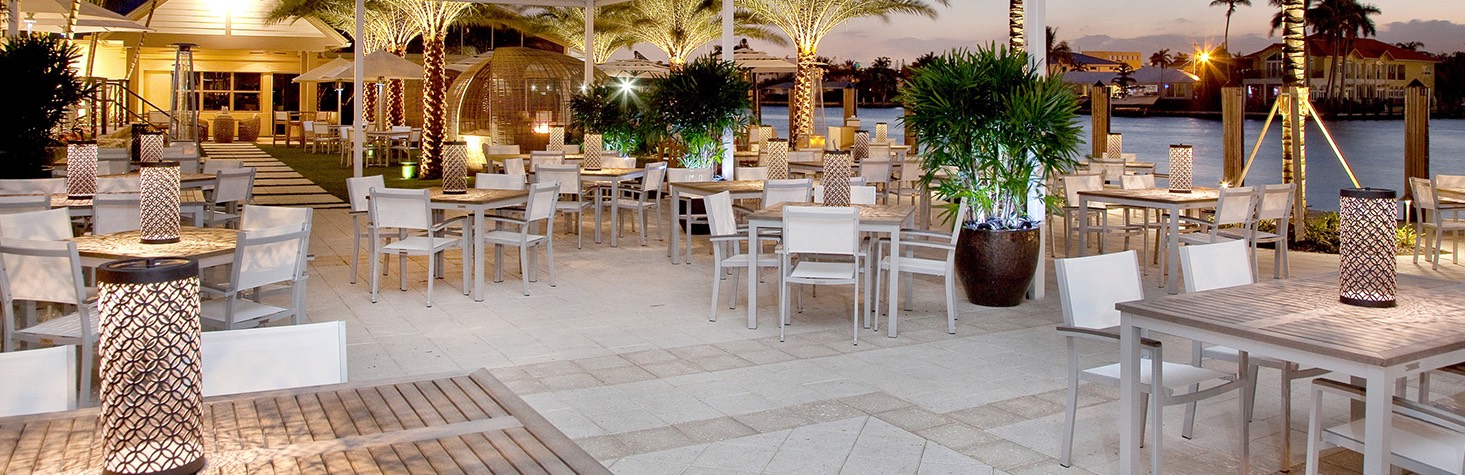 Outdoor dining area with white chairs, light wood tables and a view of the grass patio area in the rear