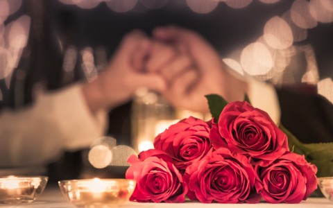 Romantic dinner with roses on the table and couple holding hands