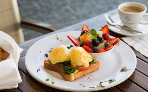 toast with hollandaise eggs with assorted fruits on white plate