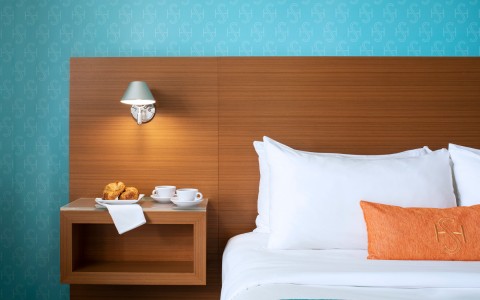  orange pillow on white bed, wooden headboard with blue wall and a night stand 