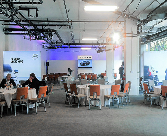 A meeting room with round tables and two people sitting in orange chairs attending a Volvo event