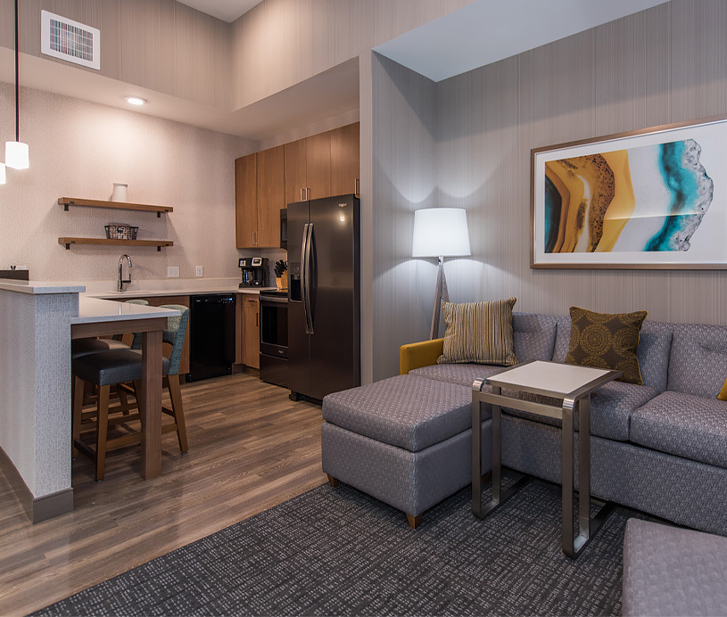 The living room has a couch and opens up next to the kitchen that features a refrigerator, barstool seating, sink, and additional kitchen appliances.  
