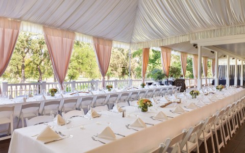 outdoor reception venue under deck with long tables and pink curtains 