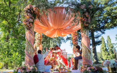 groom going to hug bride under beautiful pink and floral cabana