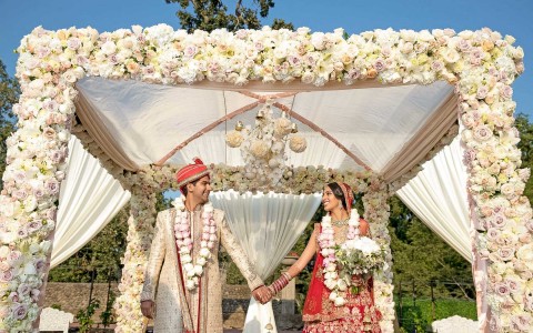 bride and groom stand under cabana decorated with flowers on the outside 