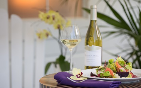 close up of white wine bottle and glass with greens on a plate 