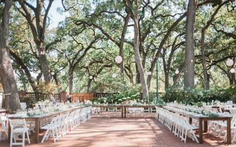 outdoor reception area with long tables and white decor and trees in the background 
