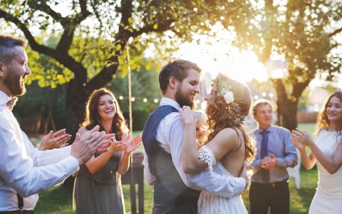 bride and groom dance with the sun behind them and people cheering them on 