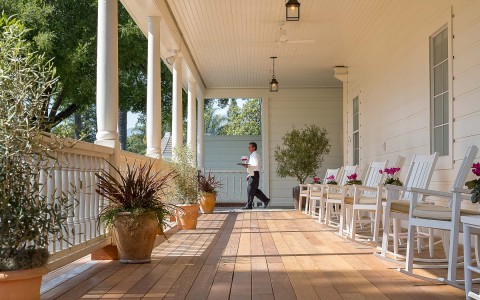 deck area with white chairs and a man walking in the background 