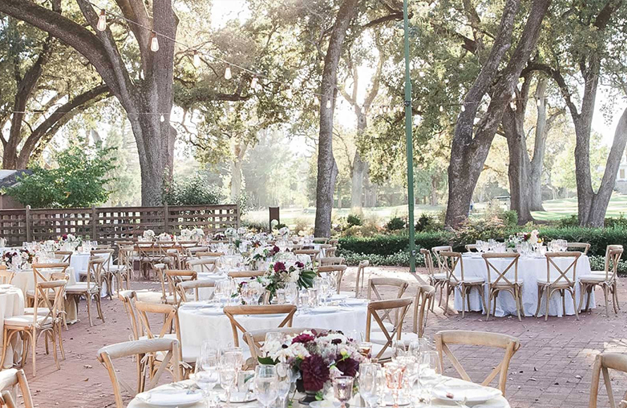 beautiful seating area under the shade of trees and decorated with red and white flower center pieces