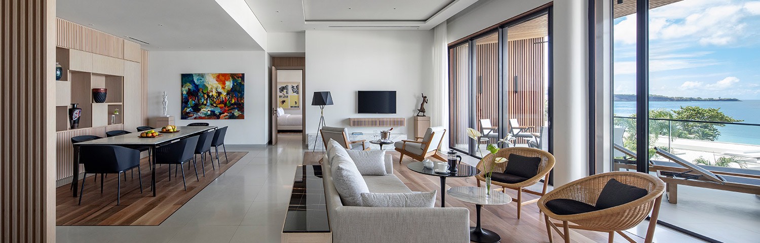 Lounge area with a couch, chairs, tv, and a long rectangular dining table surrounded by chairs in the back of the room