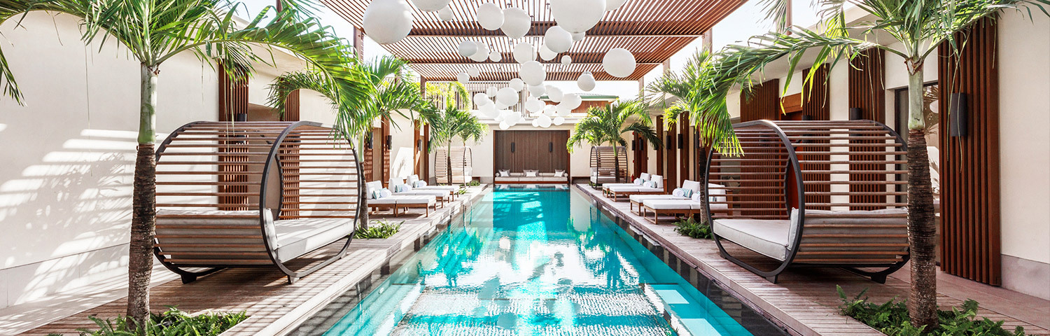 A crystal blue pool lined with palm trees and lounging chairs at the Spa in Silversands Grenada Resort
