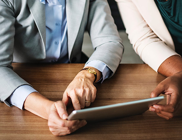 two business people sitting at a desk looking at a tablet together