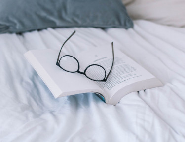 an open book with glasses on top sitting on a bed
