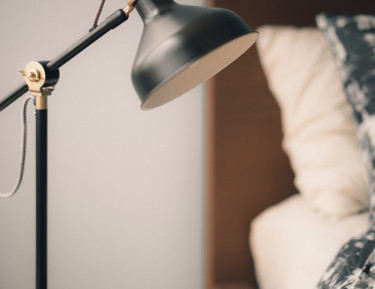 a black lamp and phone on a charger sitting on a side table next to a bed