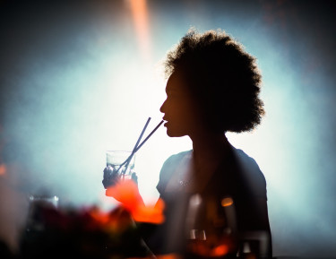 a woman sipping on a drink with a bright light behind her