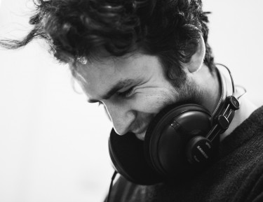 black and white image of a man wearing headphones looking down and smiling