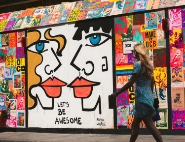 a woman walks next to a colorful wall with various murals and posters