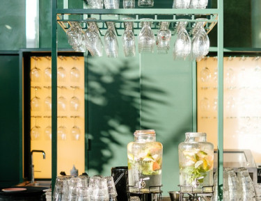 bar area with green accent colors, glassware hanging from a rack, and two pitchers of fruit infused water