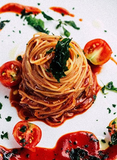 a fancy plate of pasta with sliced tomatoes and sauce drizzled on the plate