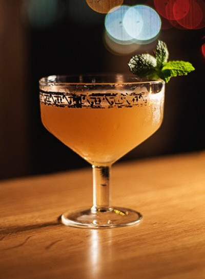 a cocktail on a wooden bar top garnished with a mint leaf