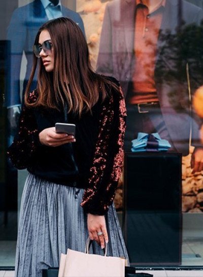 a woman standing on a sidewalk in front of mannequins in a store window while holding a shopping bag